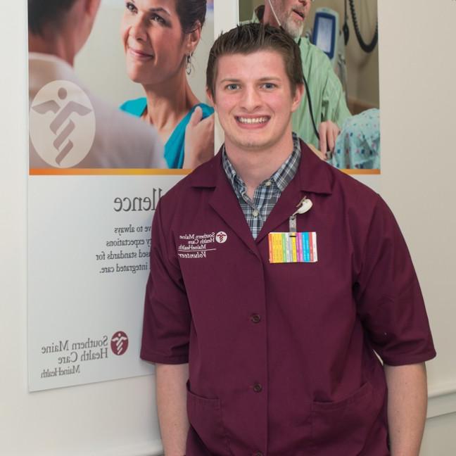 A U N E student wearing a colorful badge stands in front of a Southern Maine Health Care poster